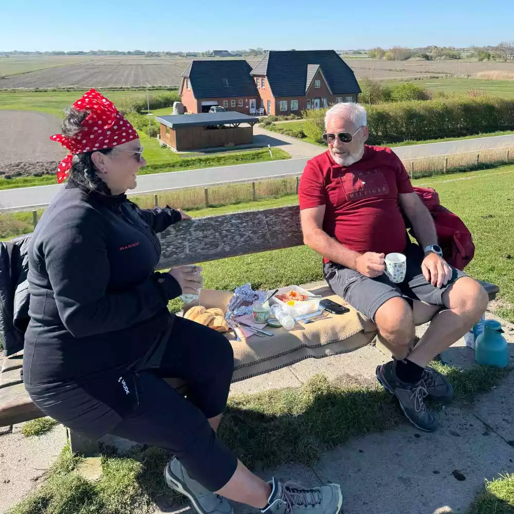 Ein Pärchen macht Picknick auf einer Bank am Deich und geniesst den Urlaub zu zweit